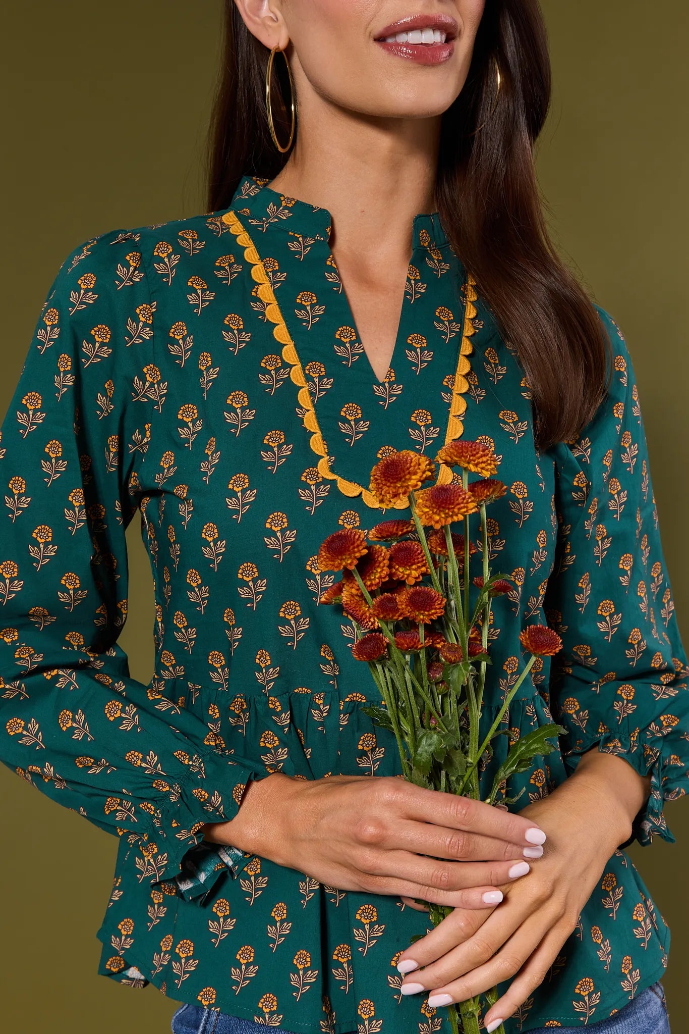 Woman wearing a green floral Fallon Top holding flowers against a dark background