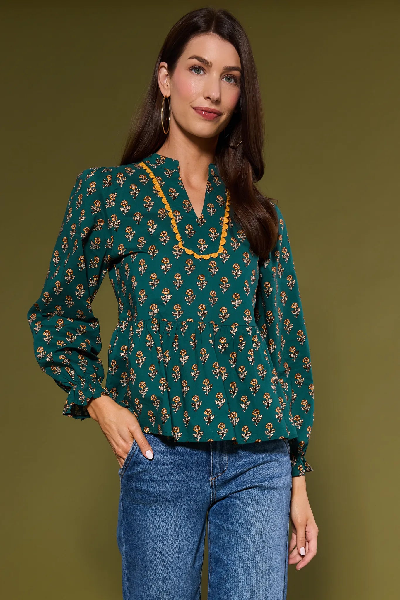 Woman wearing a green patterned Fallon Top with blue jeans against a green background