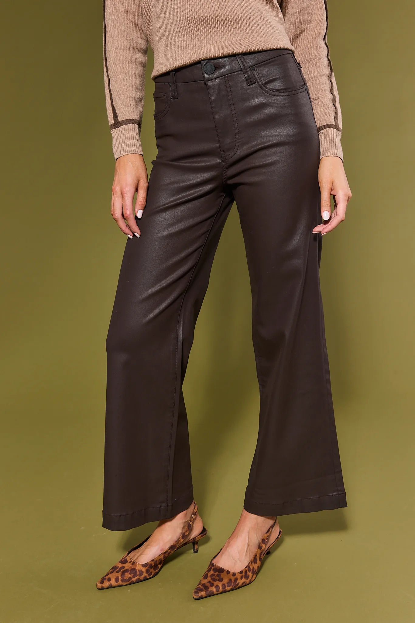 Person wearing brown Meg Jeans Wax Coated with a beige sweater and leopard print shoes on a green background