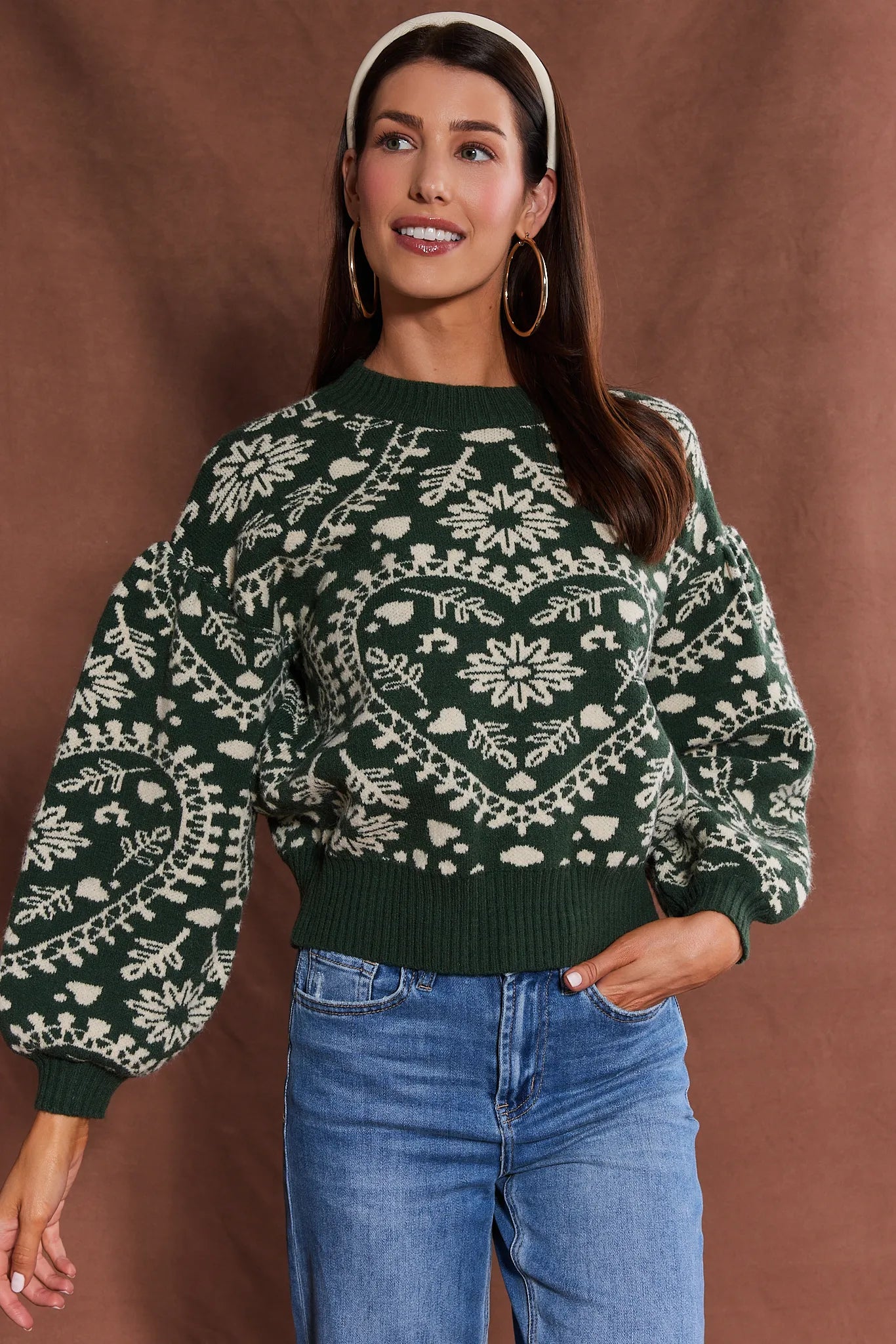 Woman wearing a green patterned Pamela Sweater and blue jeans against a brown background