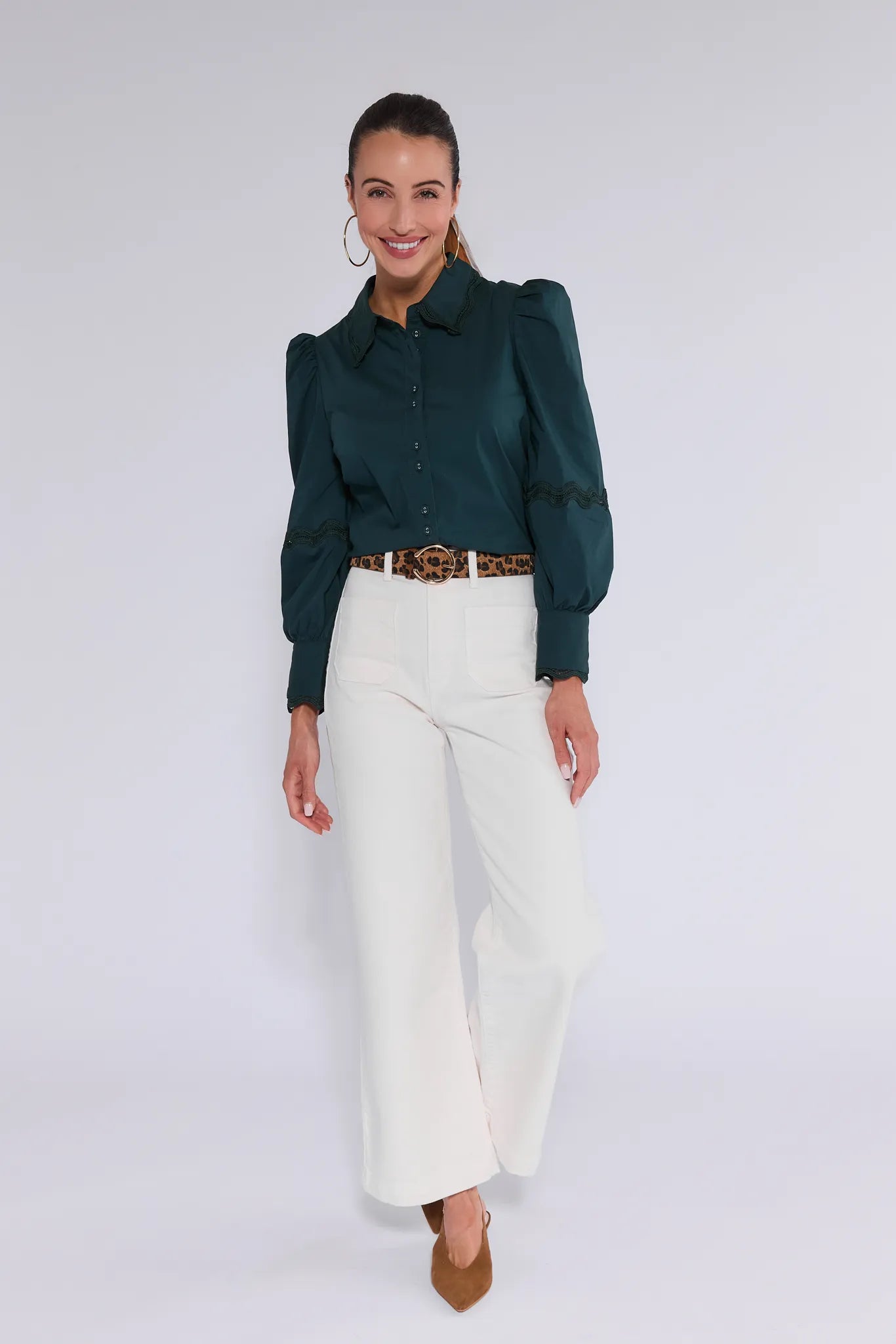 Woman wearing a dark green Ellis Top and white pants with a belt on a white background