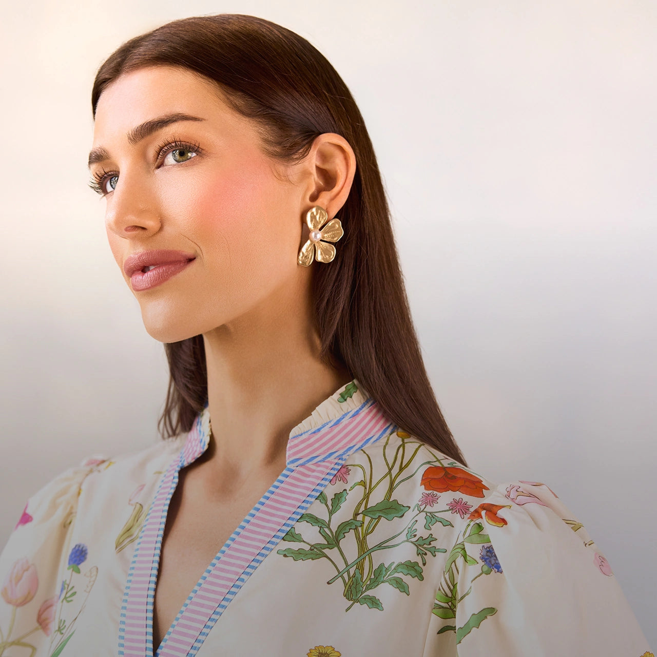 Woman wearing gold floral earrings with a neutral background