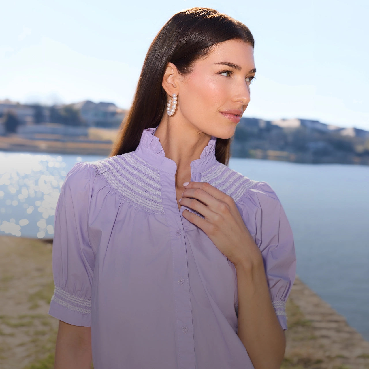 Woman wearing a light purple blouse with lace details by a lake