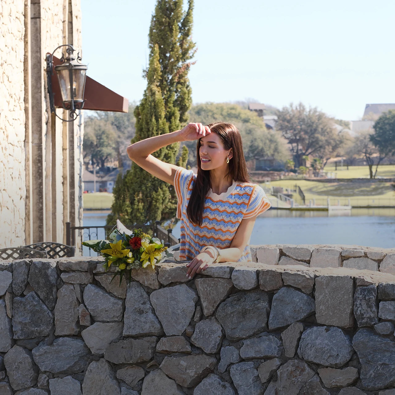 Woman standing by a stone wall with a scenic background