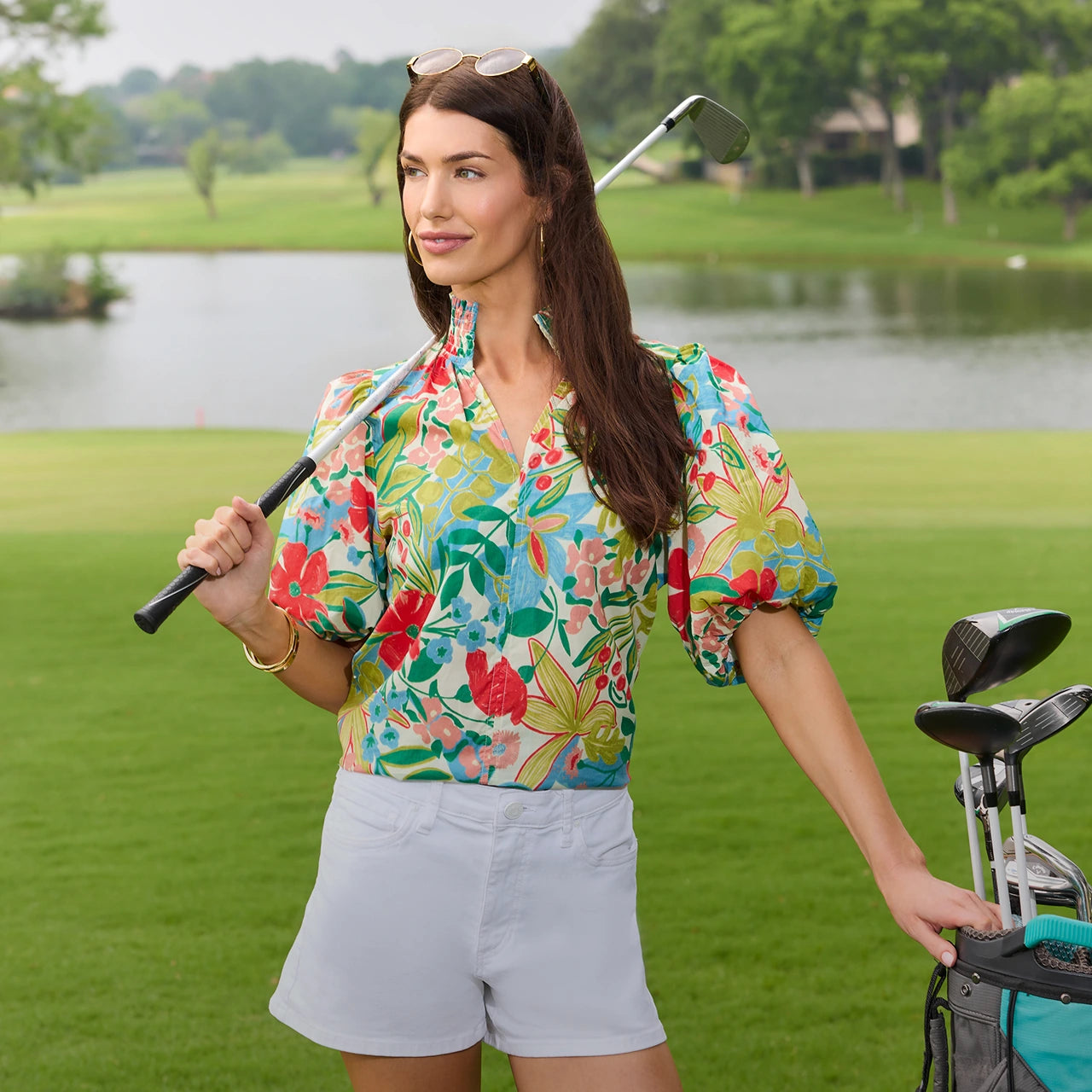 Woman in a colorful floral shirt holding a golf club on a golf course with a lake in the background. desktop