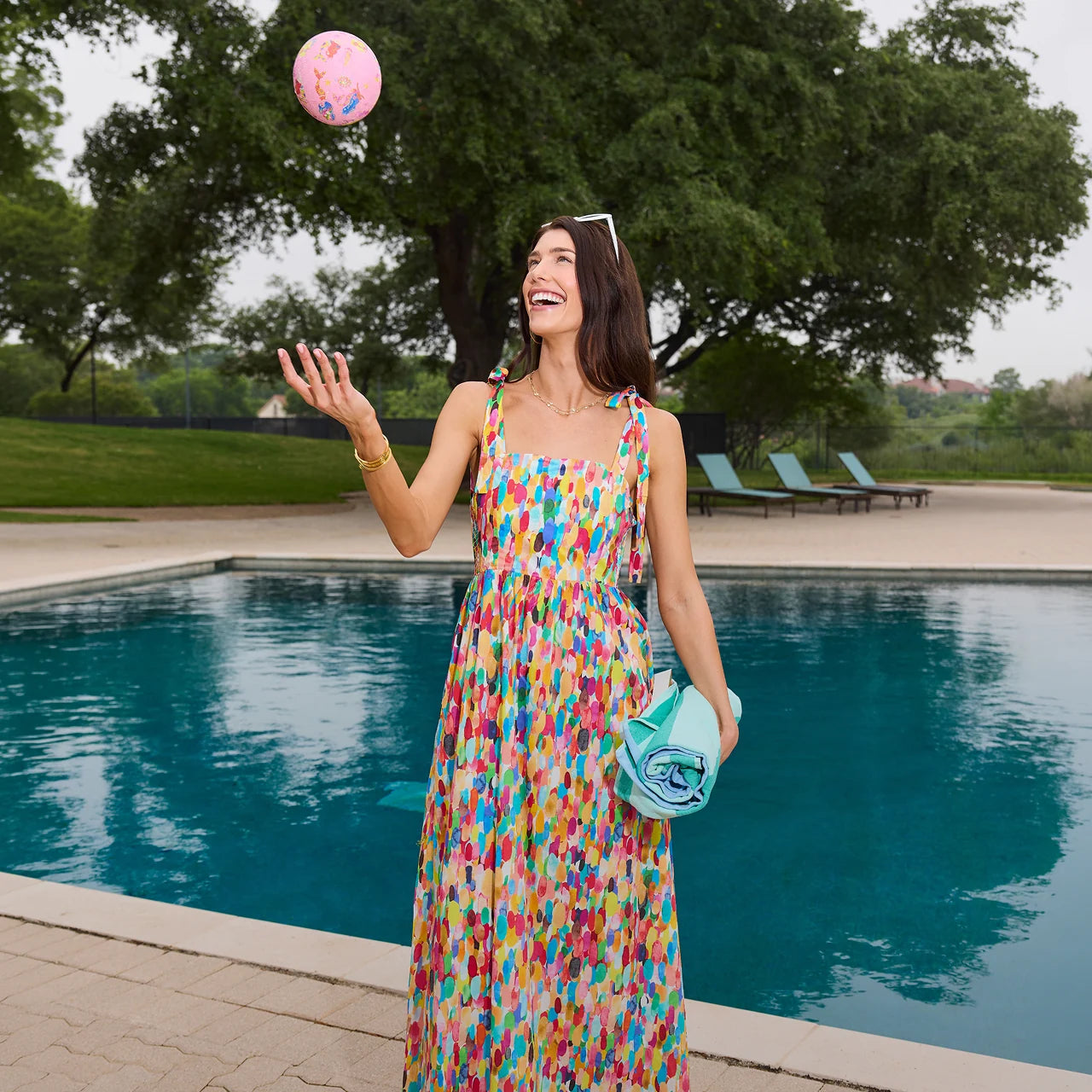 Woman in a colorful dress juggling a pink ball by a pool collection