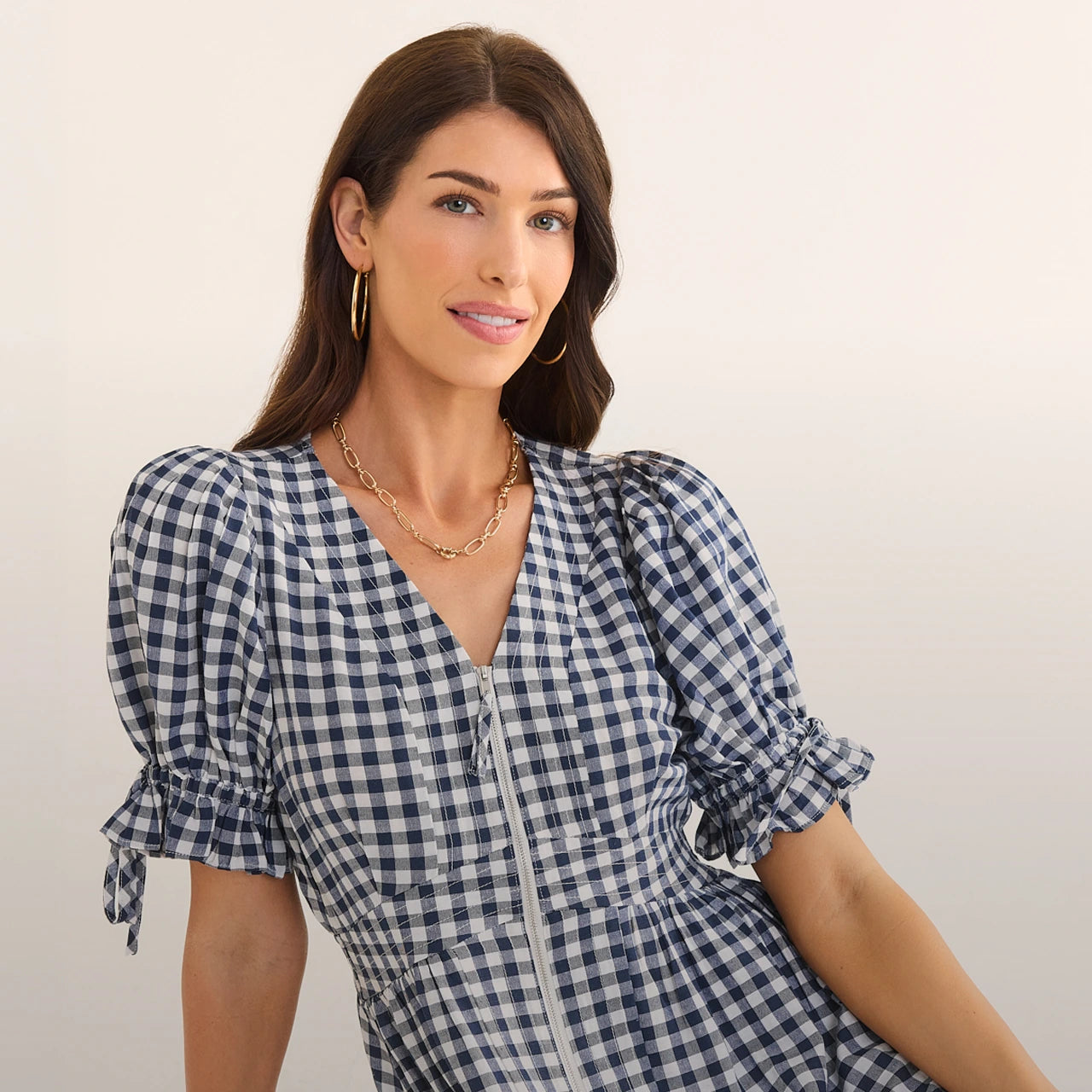 Woman wearing a blue and white checkered dress with a plain background hero