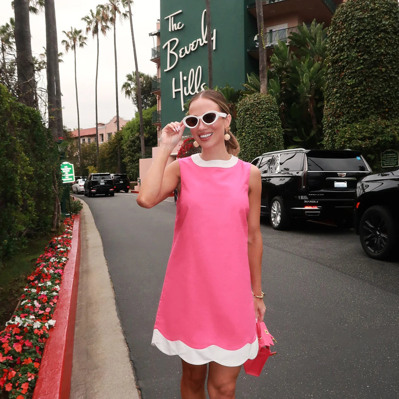 Woman in a pink dress standing on a street with 'The Beverly Hills' sign in the background. collection