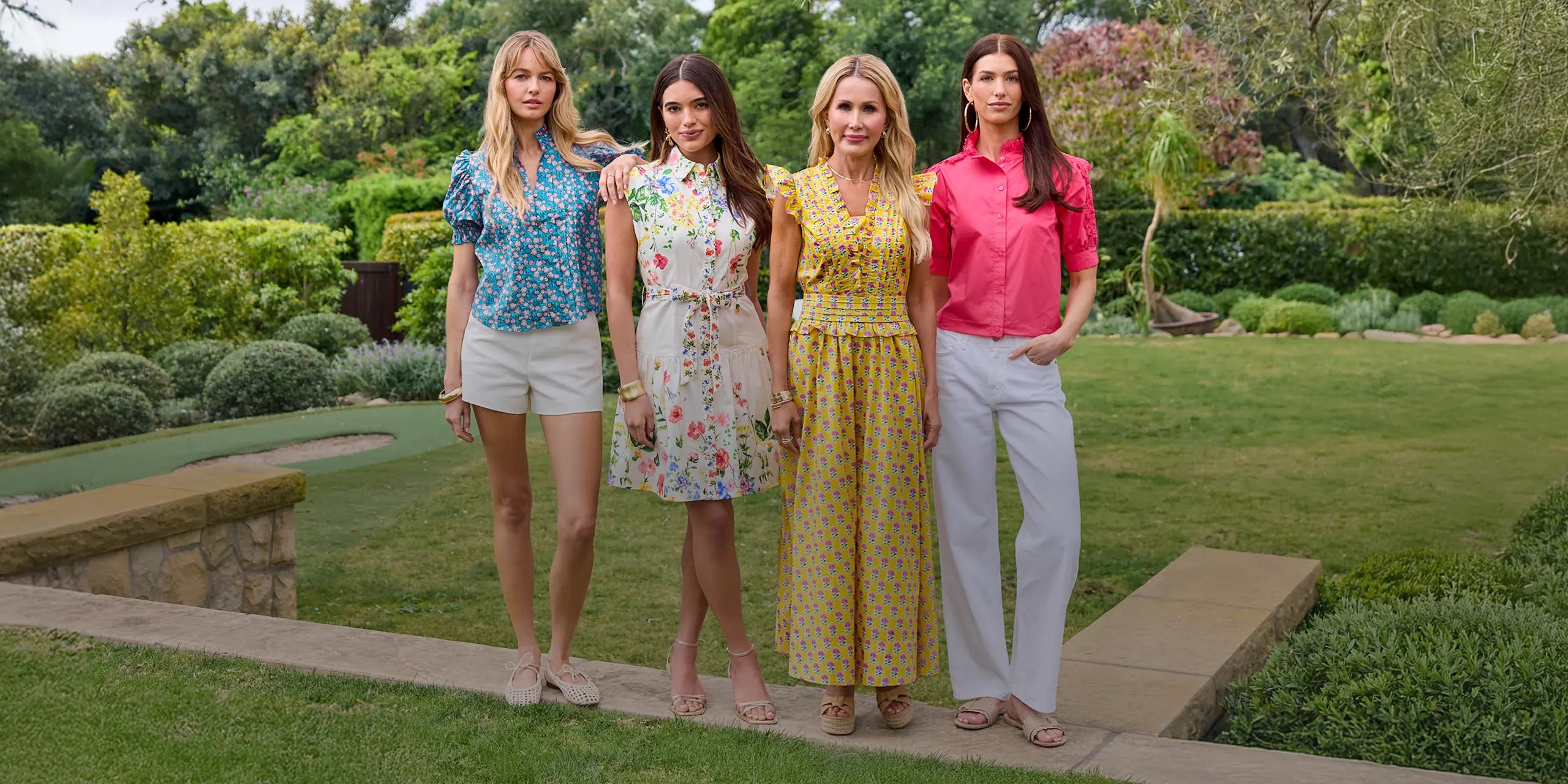 Four women standing on a garden path with greenery in the background