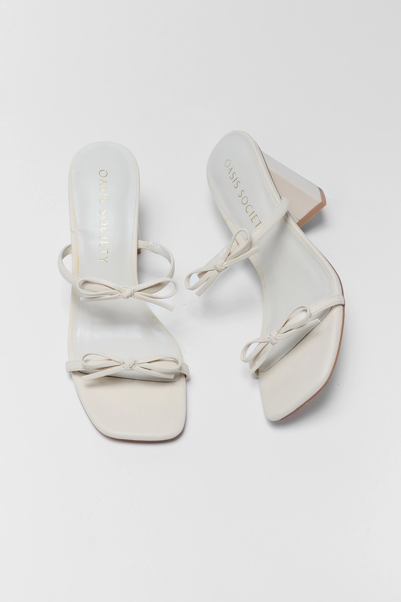 Pair of white sandals with bow details on a light gray background