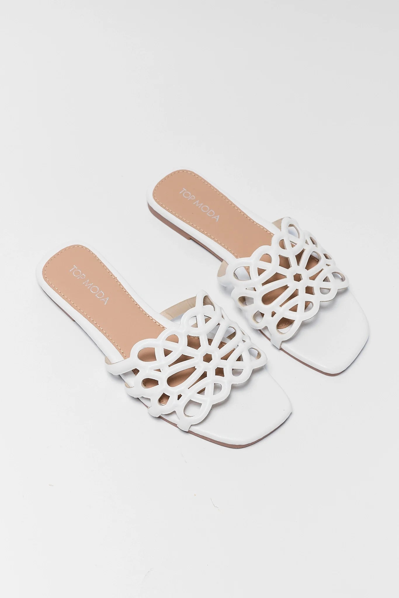 White sandals with intricate cut-out design on a light gray background
