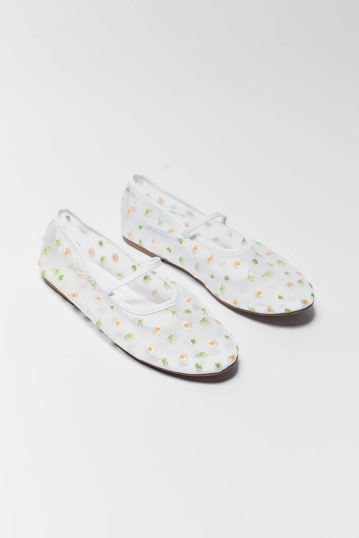 Pair of white loafers with floral pattern on a light gray background