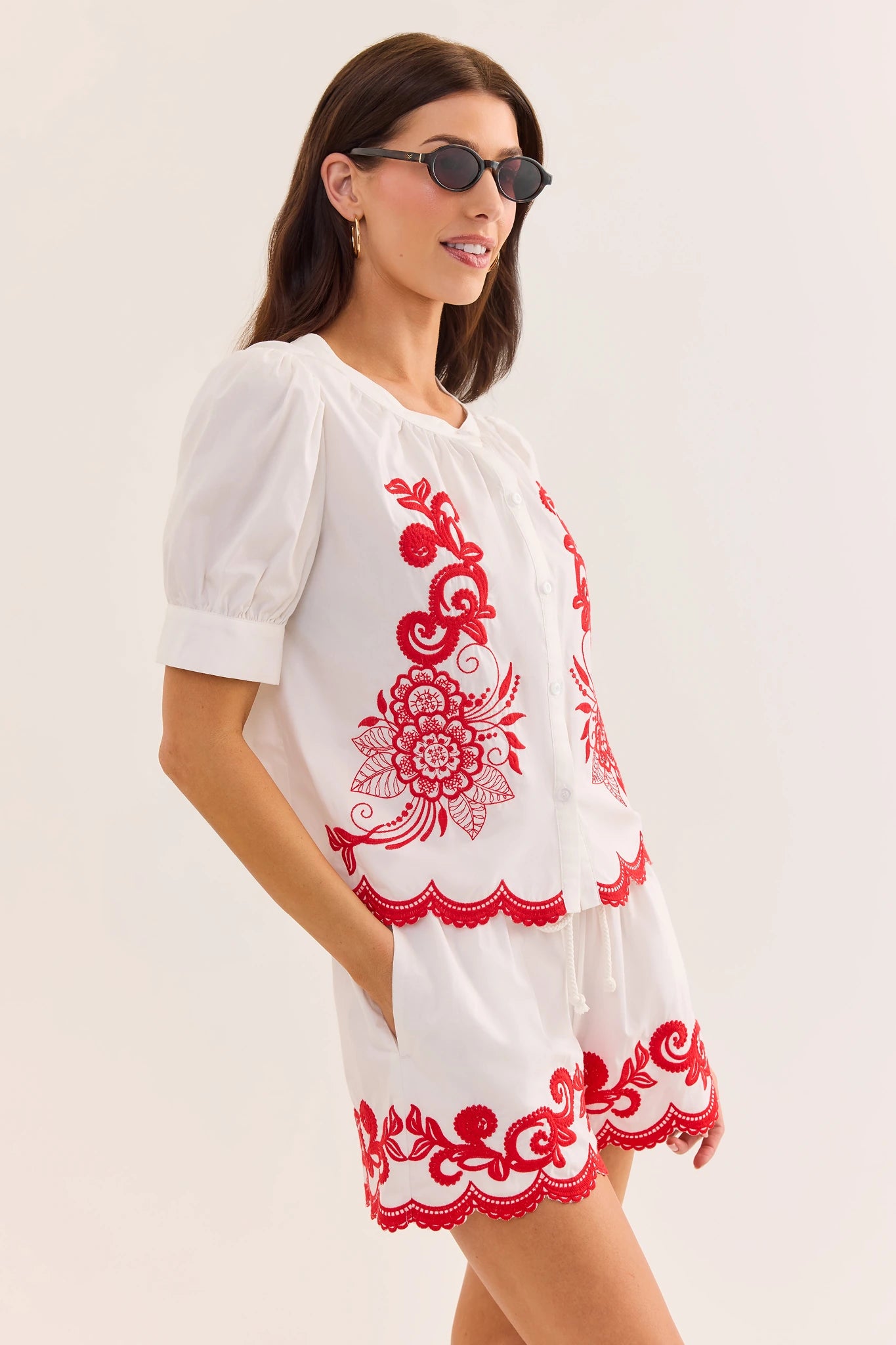 lifestyle Woman wearing a white dress with red floral embroidery on a plain background