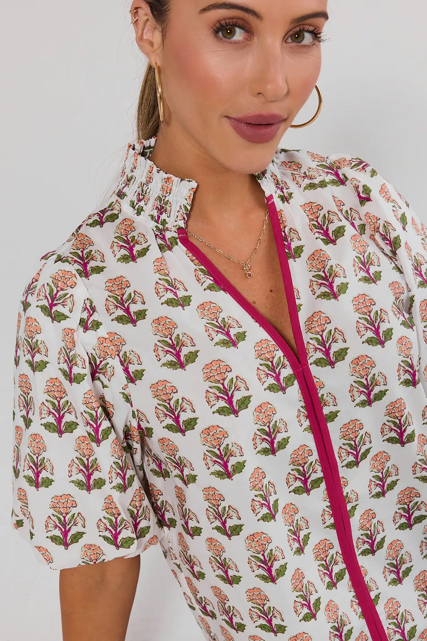A close-up of a woman wearing a white short-sleeve blouse with a pink and green floral block print and a bright pink zipper trim.