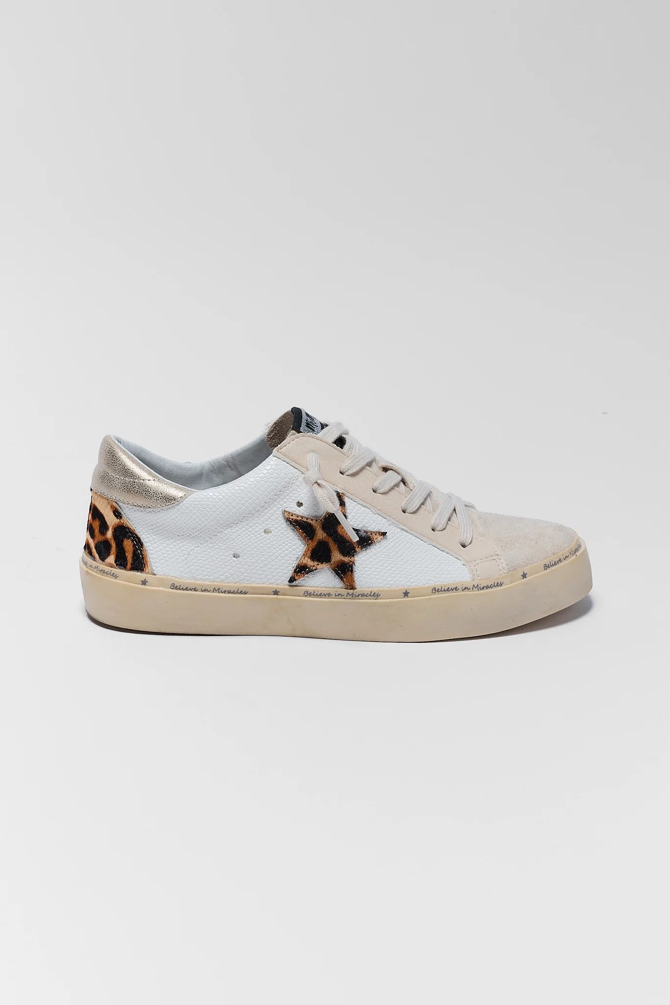 A white leather sneaker featuring a star-shaped leopard print patch on the side, a leopard print heel tab, and a beige rubber sole, shown against a light gray background.