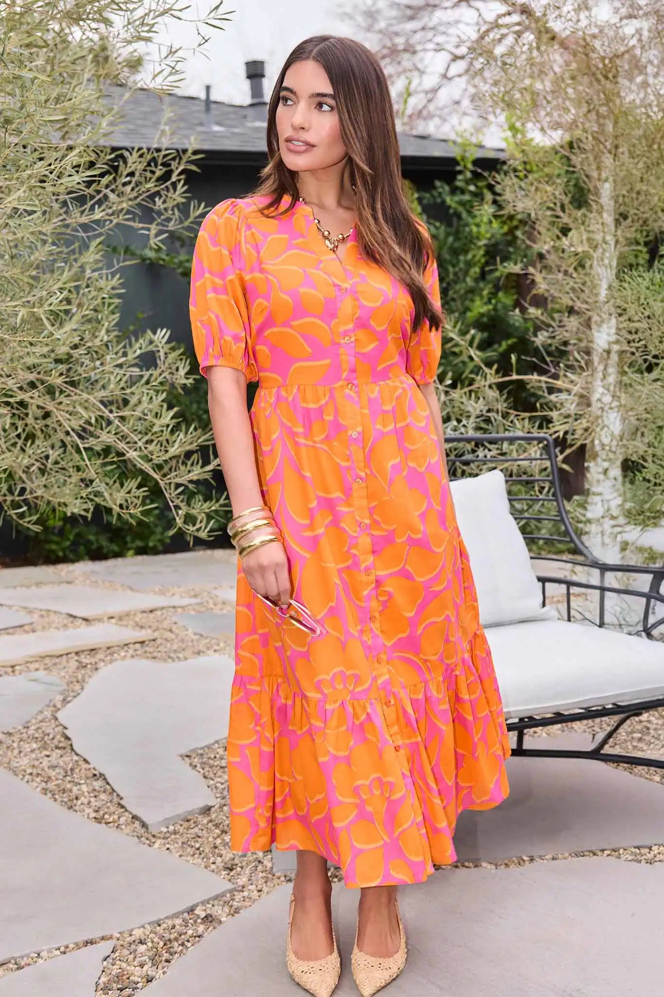 Woman in an orange and pink dress standing outdoors.