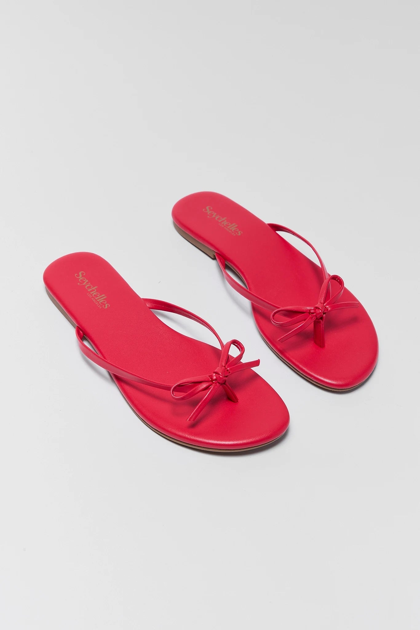 two Red sandals with a bow on a light gray background