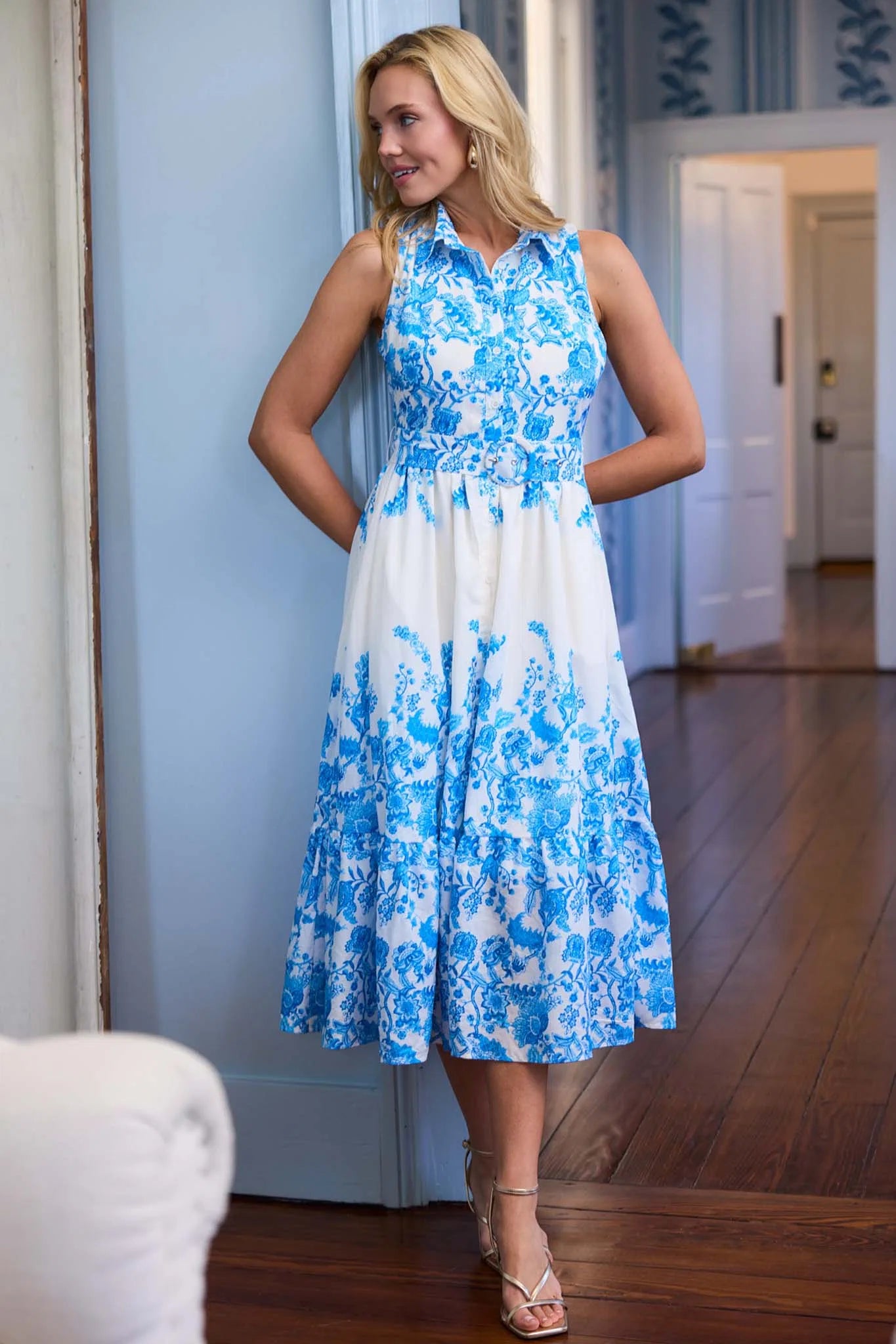 Woman wearing a blue and white floral dress in a room with wooden flooring.