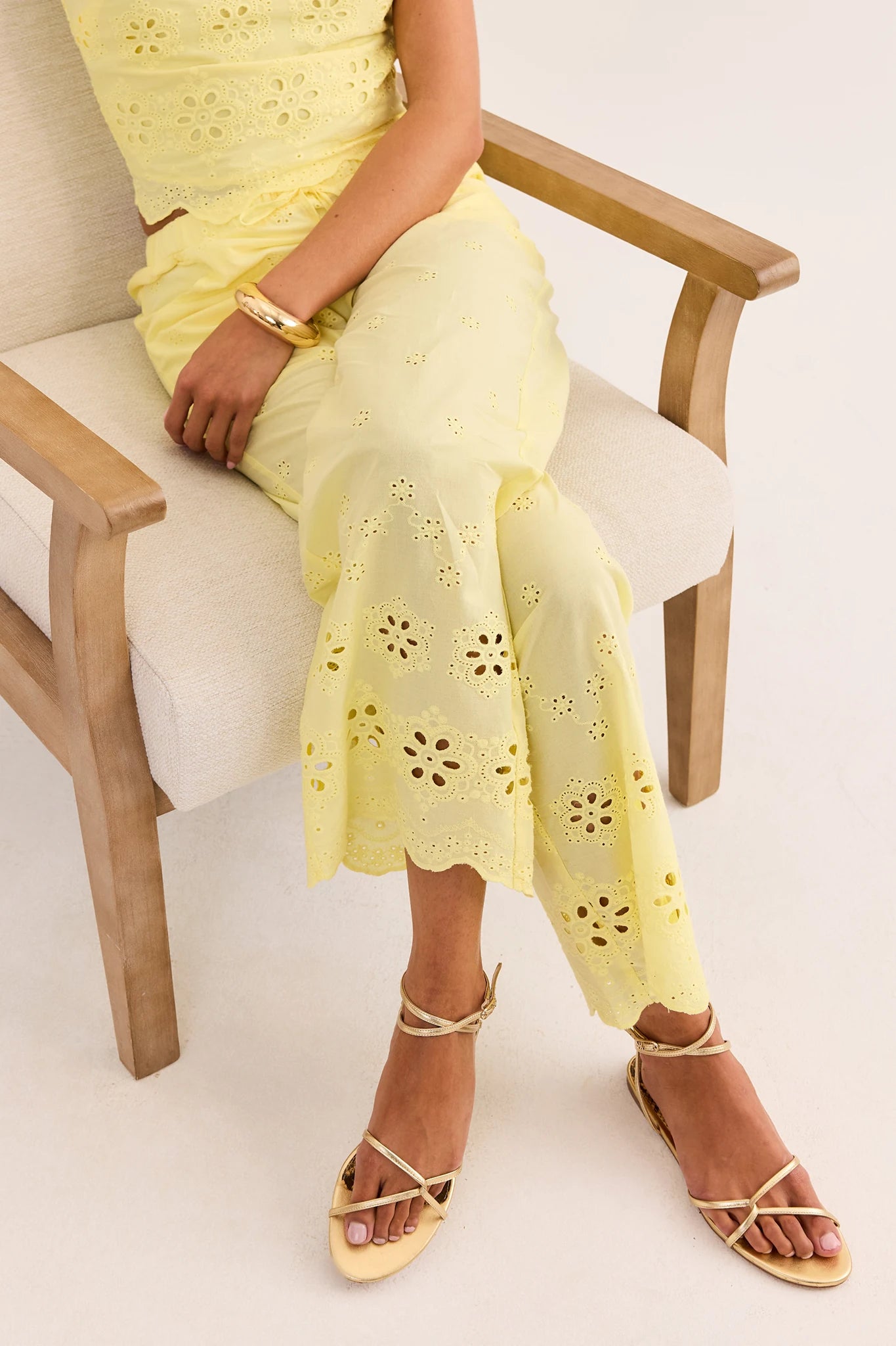 Person wearing a yellow pant with floral cut-out pattern sitting on a chair.