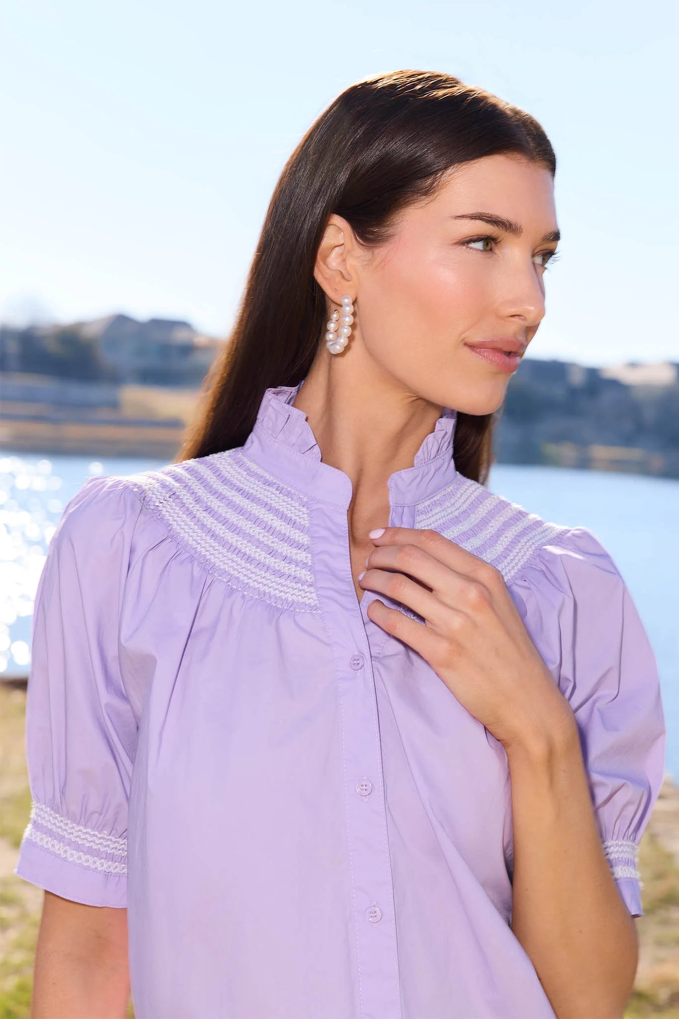 Woman wearing a light purple blouse with lace details by a body of water.
