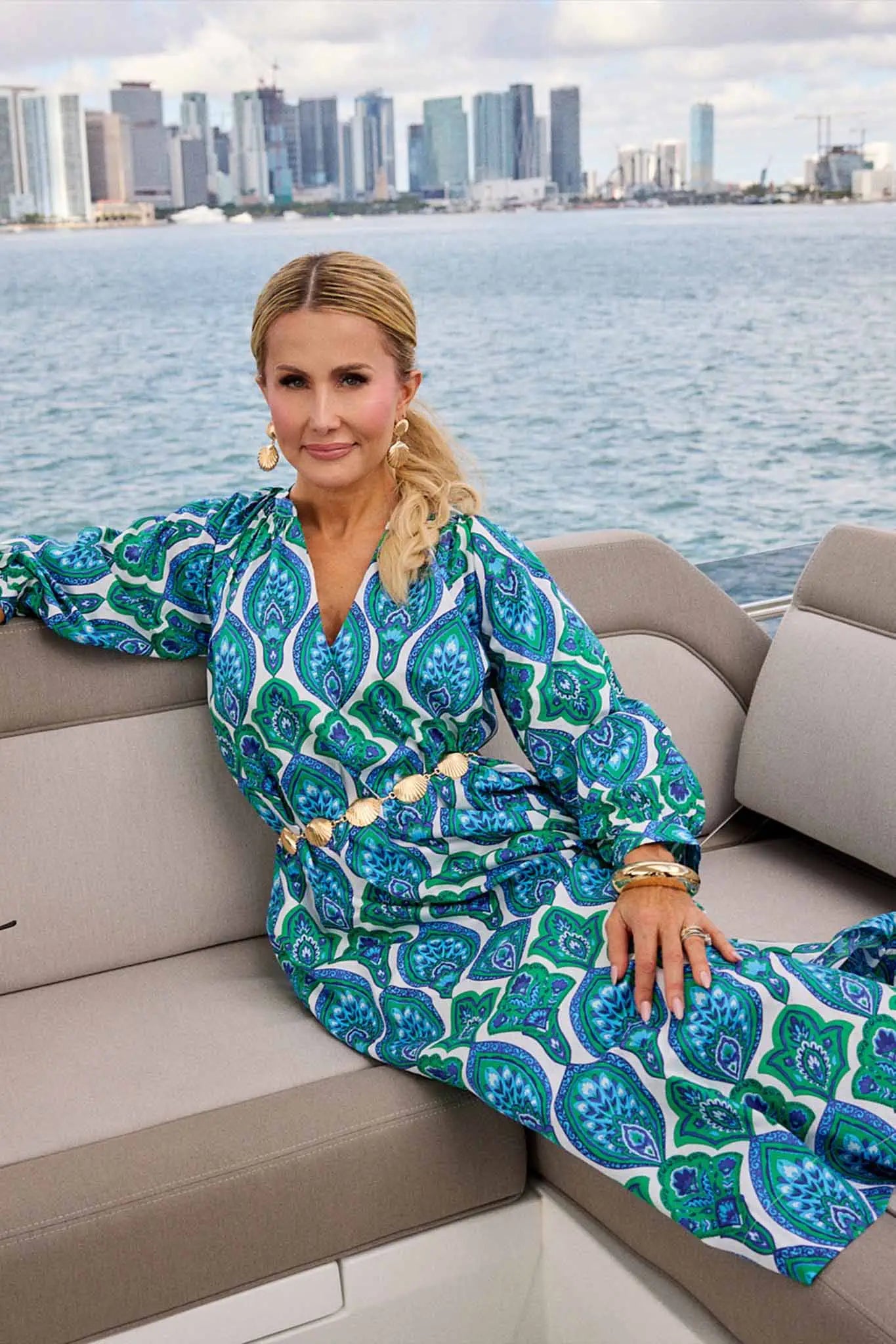 Woman in a blue patterned outfit sitting on a boat with a city skyline in the background