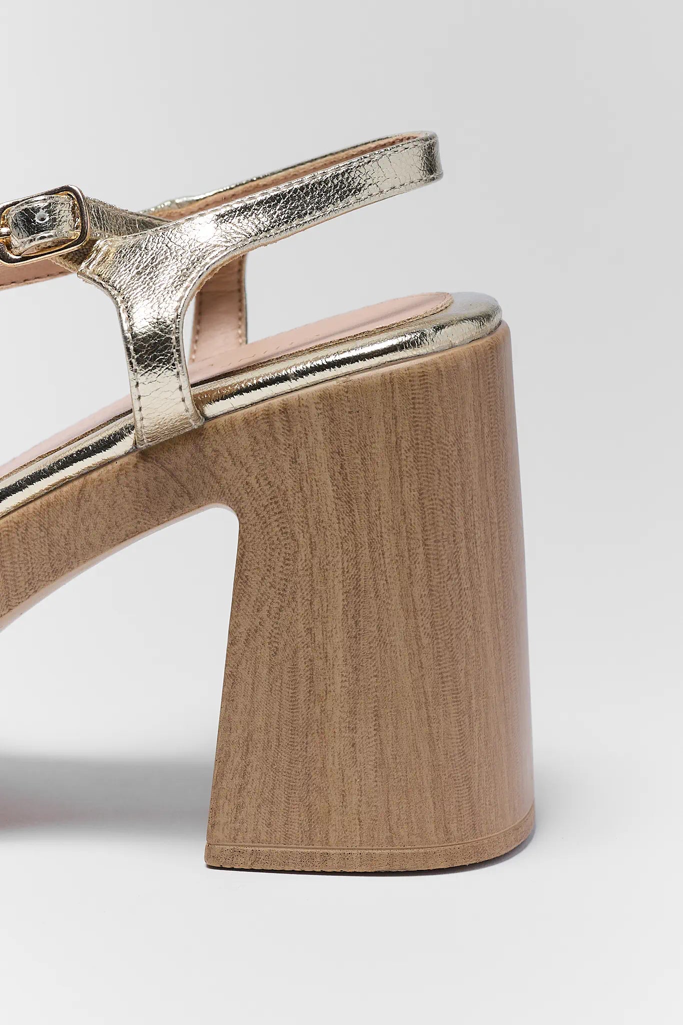 Close-up of a sandal with gold strap and beige block heel on a light gray background