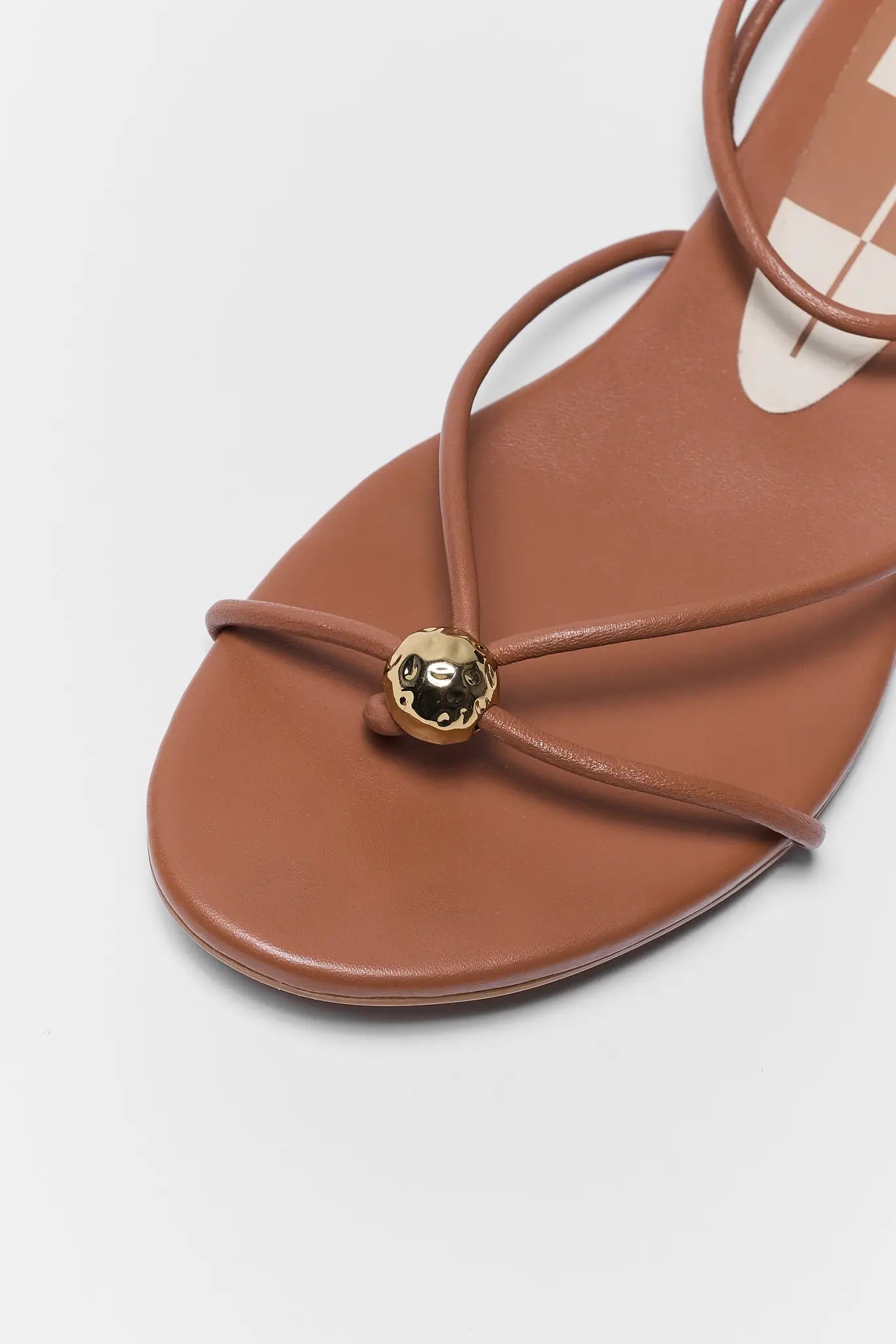 Brown sandal with a gold embellishment on a light gray background