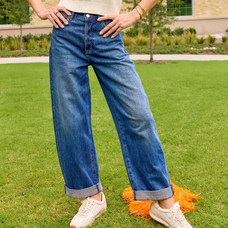 A person standing on a green lawn wearing blue wide-leg cuffed jeans, a cream knit top, and white sneakers.