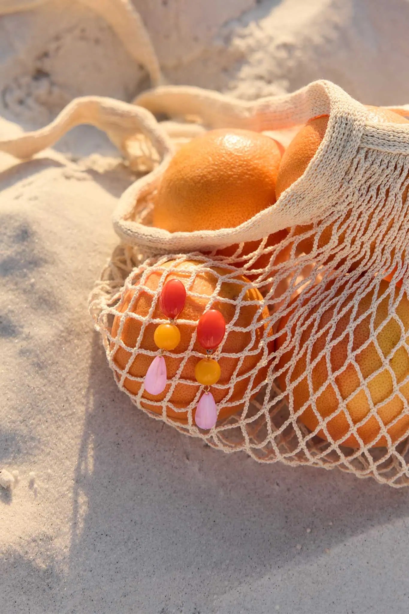 Net bag filled with oranges on a sandy surface