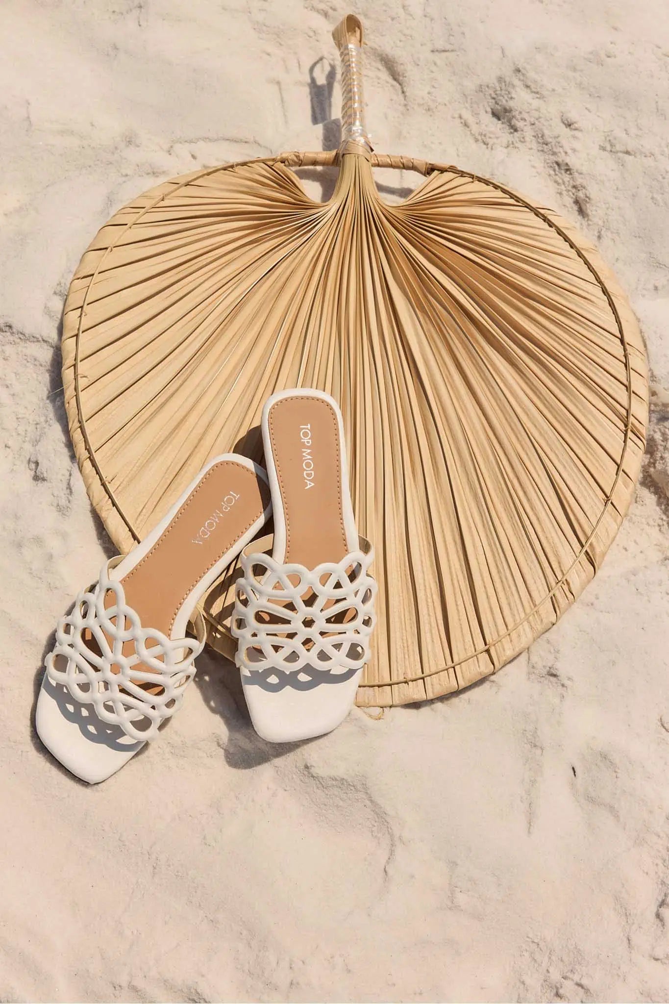 White sandals with intricate patterns on a textured surface with a large dried leaf.