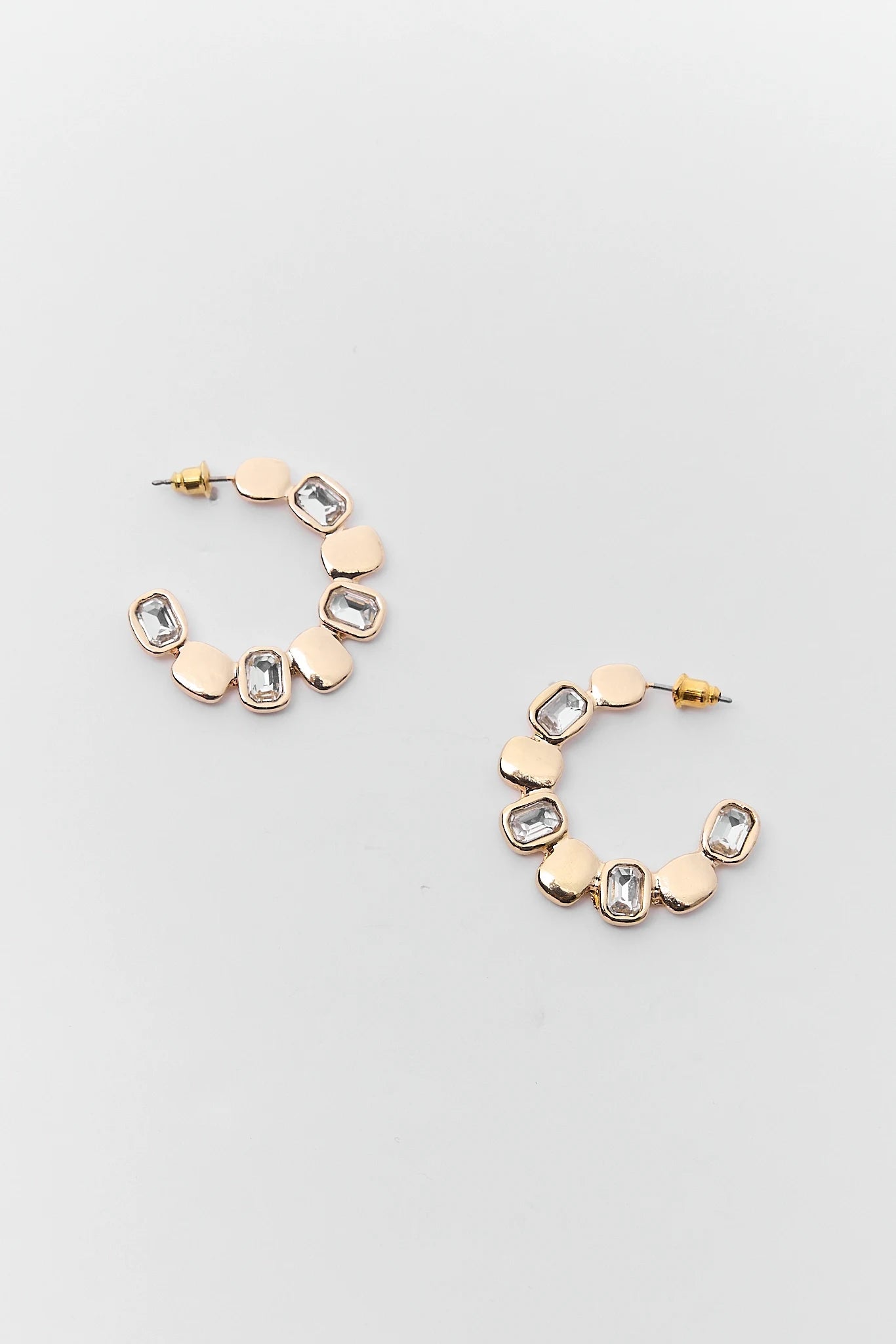 Gold and rose gold hoop earrings with geometric designs on a light gray background