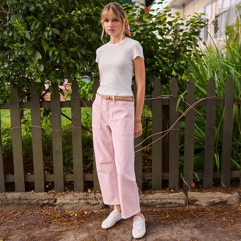 Woman wearing a white t-shirt and pink striped pants standing in front of a garden fence.