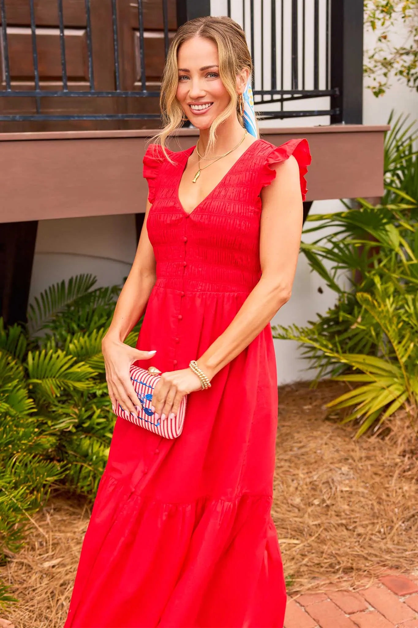 Woman in a red dress holding a clutch in an outdoor setting