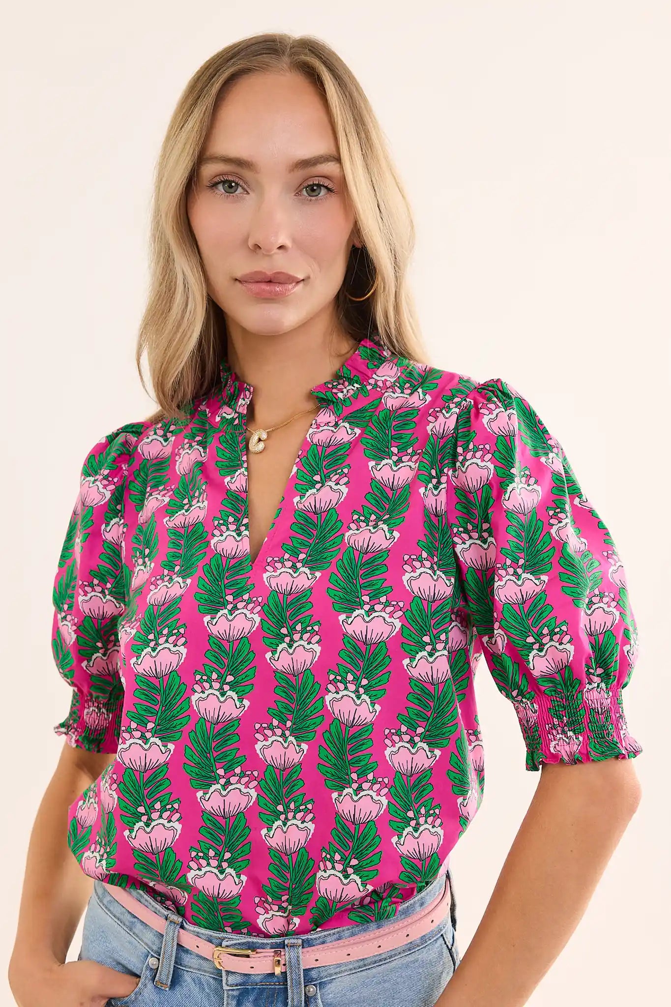 woman wearing amanda pink floral green top with jeans and pink belt on white background