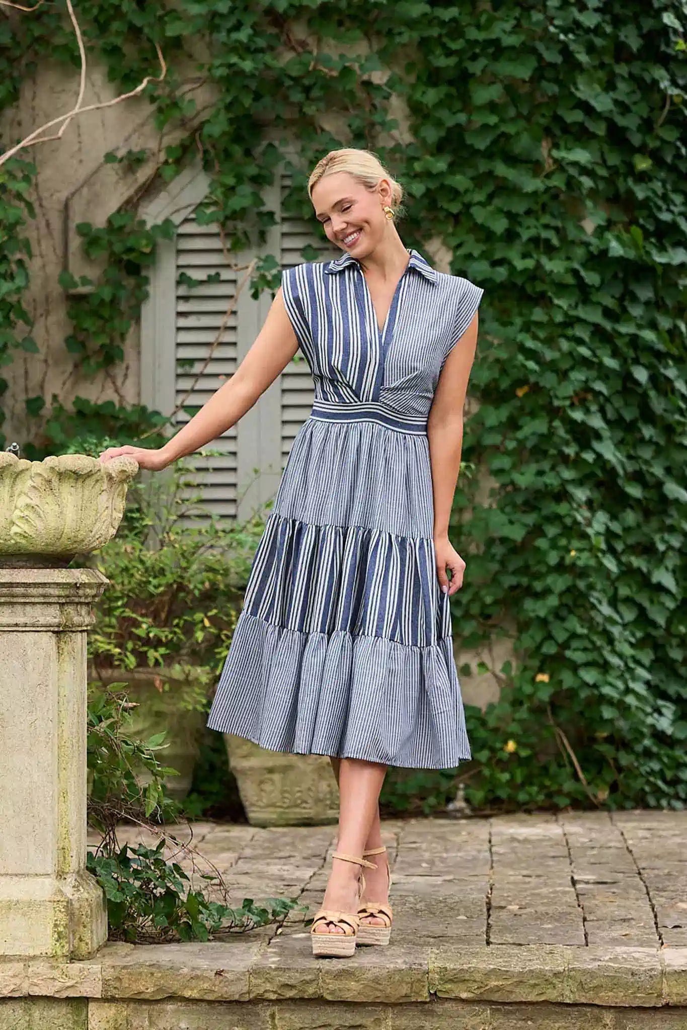 Woman in a striped dress standing outdoors with greenery in the background