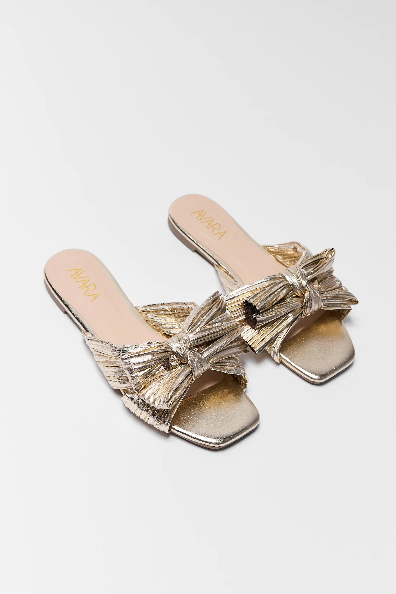 Gold sandals with bow detail on a white background