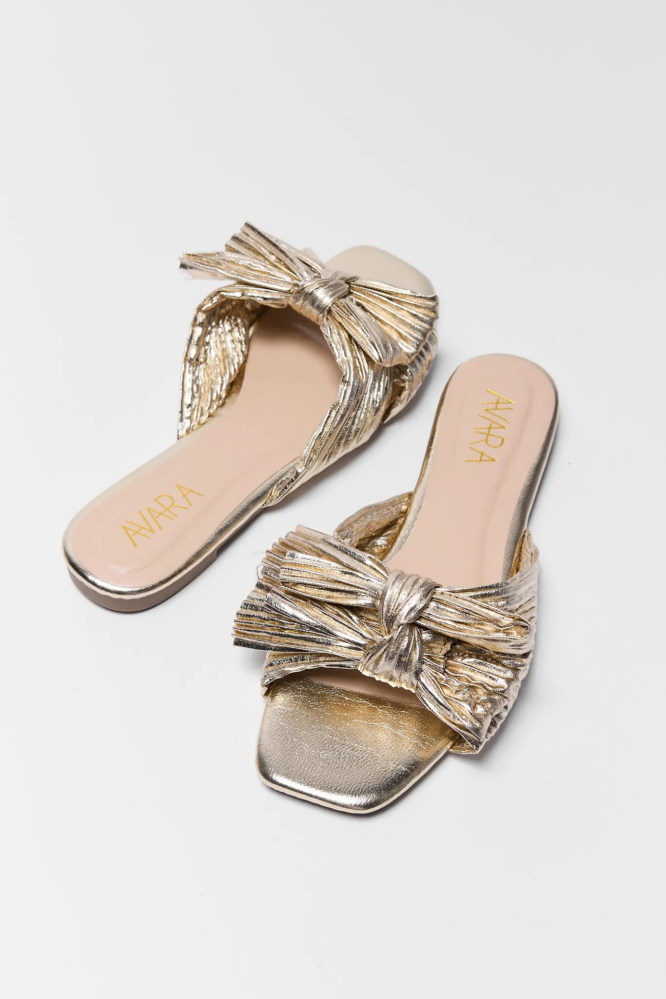 two Gold sandals with bow design on a light gray background