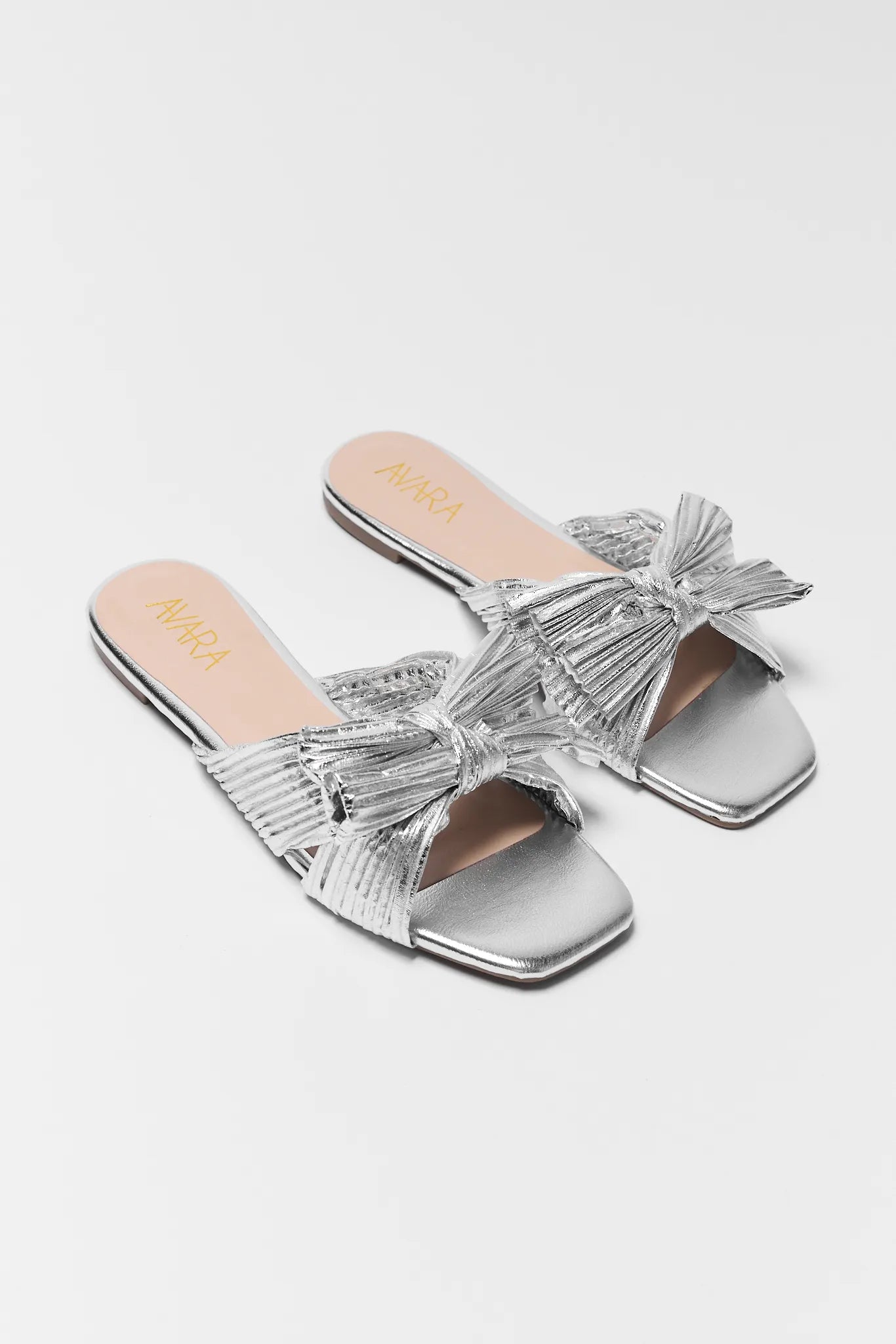 Silver sandals with bow details on a white background at angle