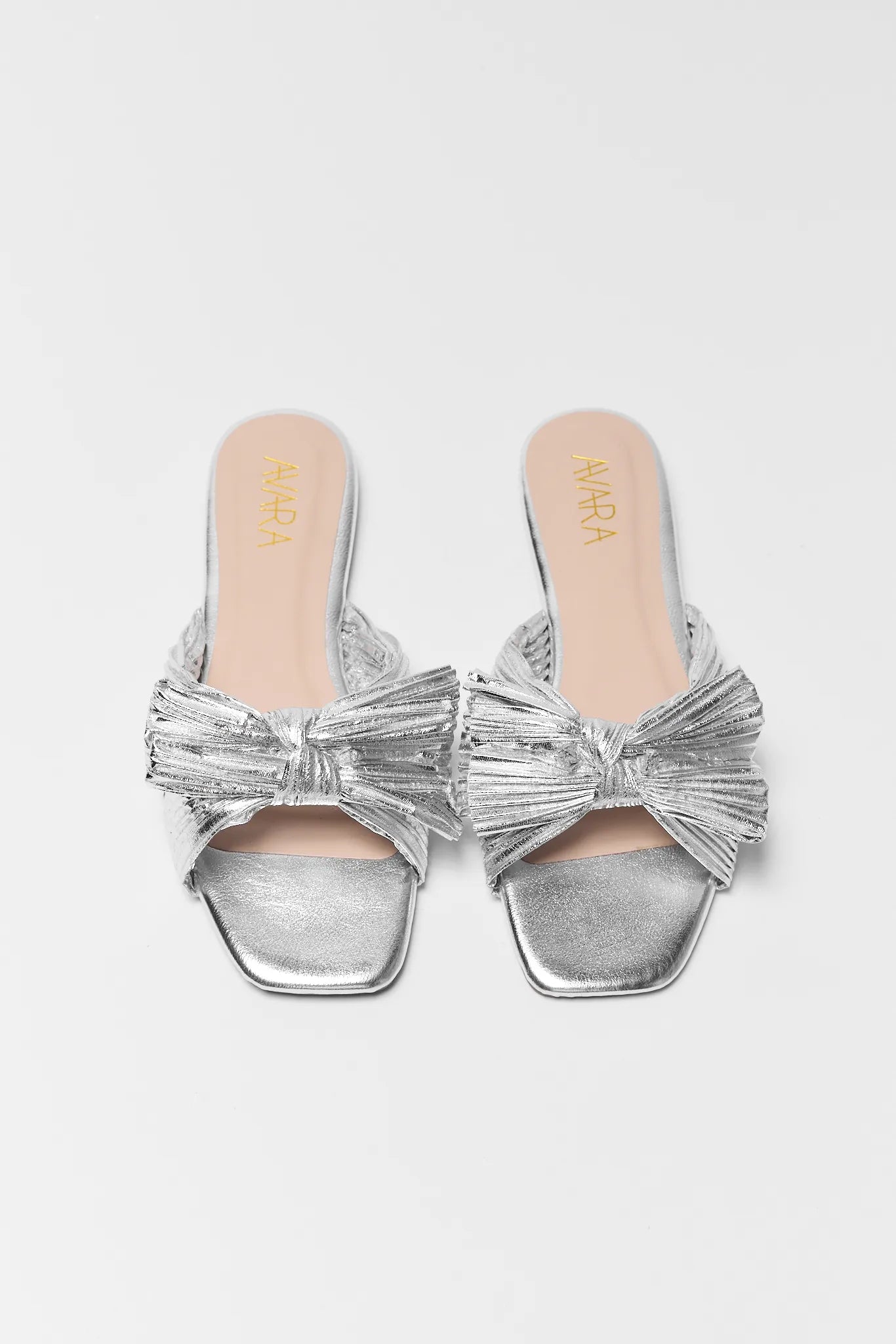 two Silver metallic sandals with bow detail on a light gray background