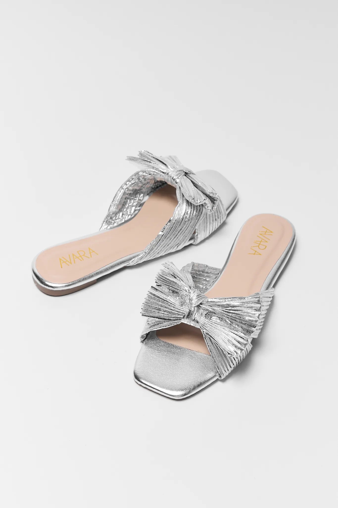 Silver sandals with bow details on a white background