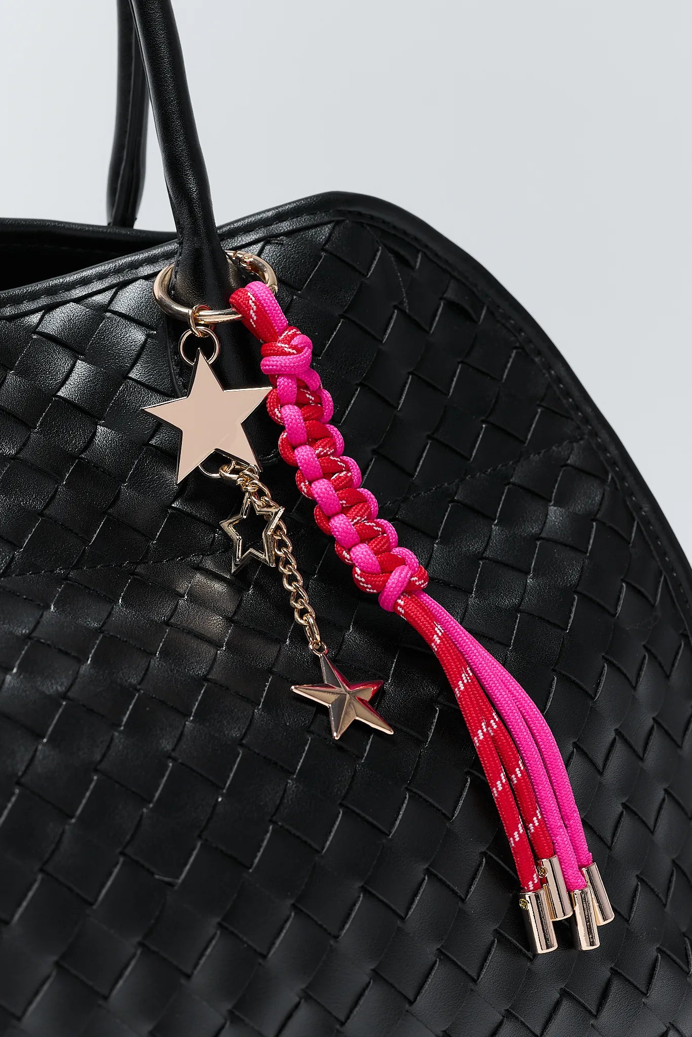 Black woven handbag with a pink braided keychain featuring star charms on a light gray background