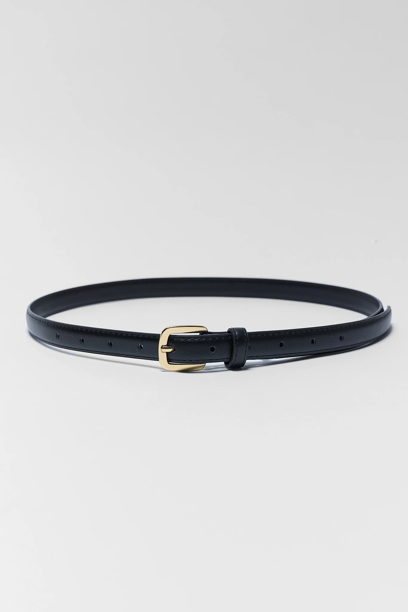 A slim black leather belt with a gold-tone buckle, coiled on a light gray background.