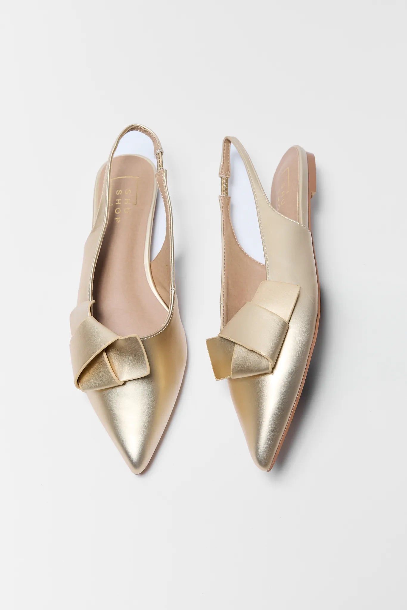 Pair of gold slingback shoes with bow details on a light gray background