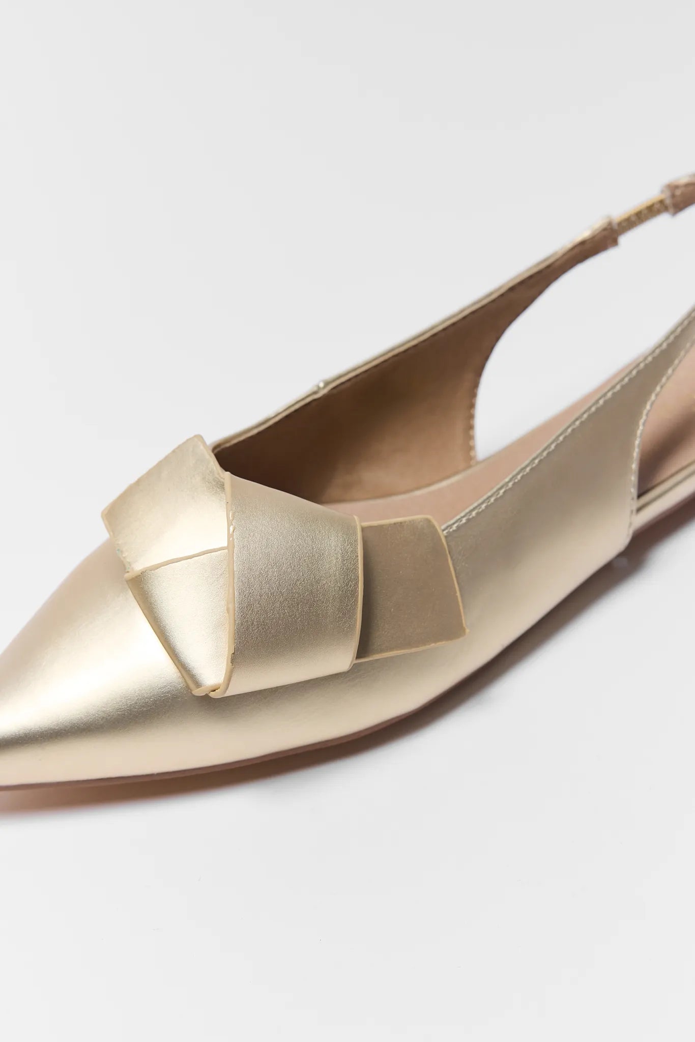 Gold pointed-toe shoe with a bow detail on a light gray background