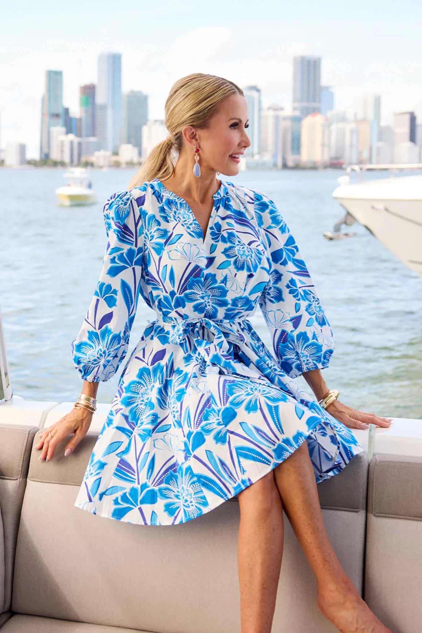 Woman in a blue floral dress sitting on a boat with a city skyline in the background