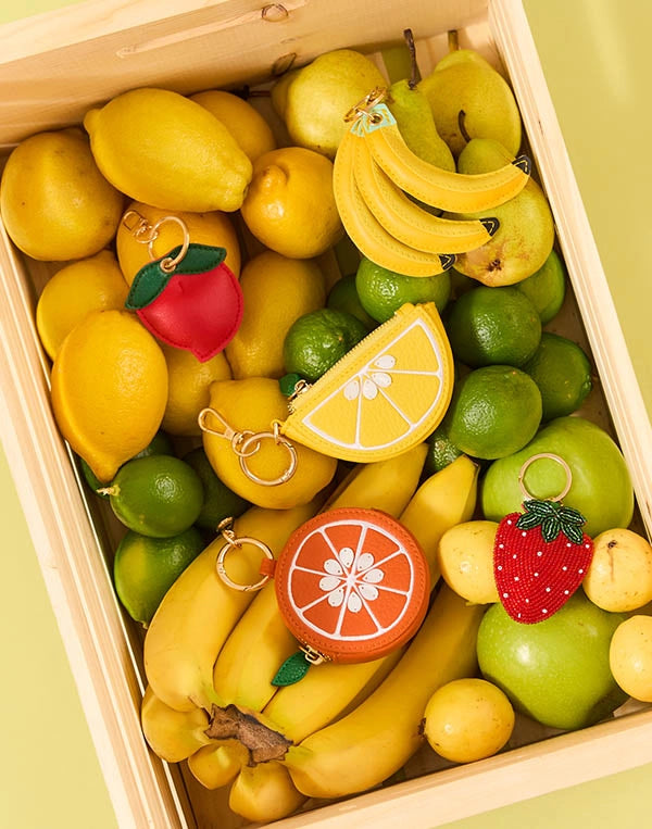 Fruit-shaped keychains in a box with lemons, limes, and bananas.