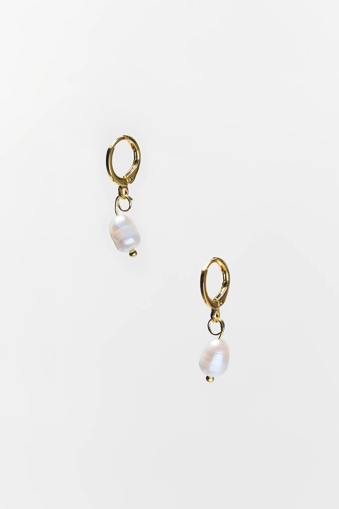 Gold earrings with pearl drops on a light beige background