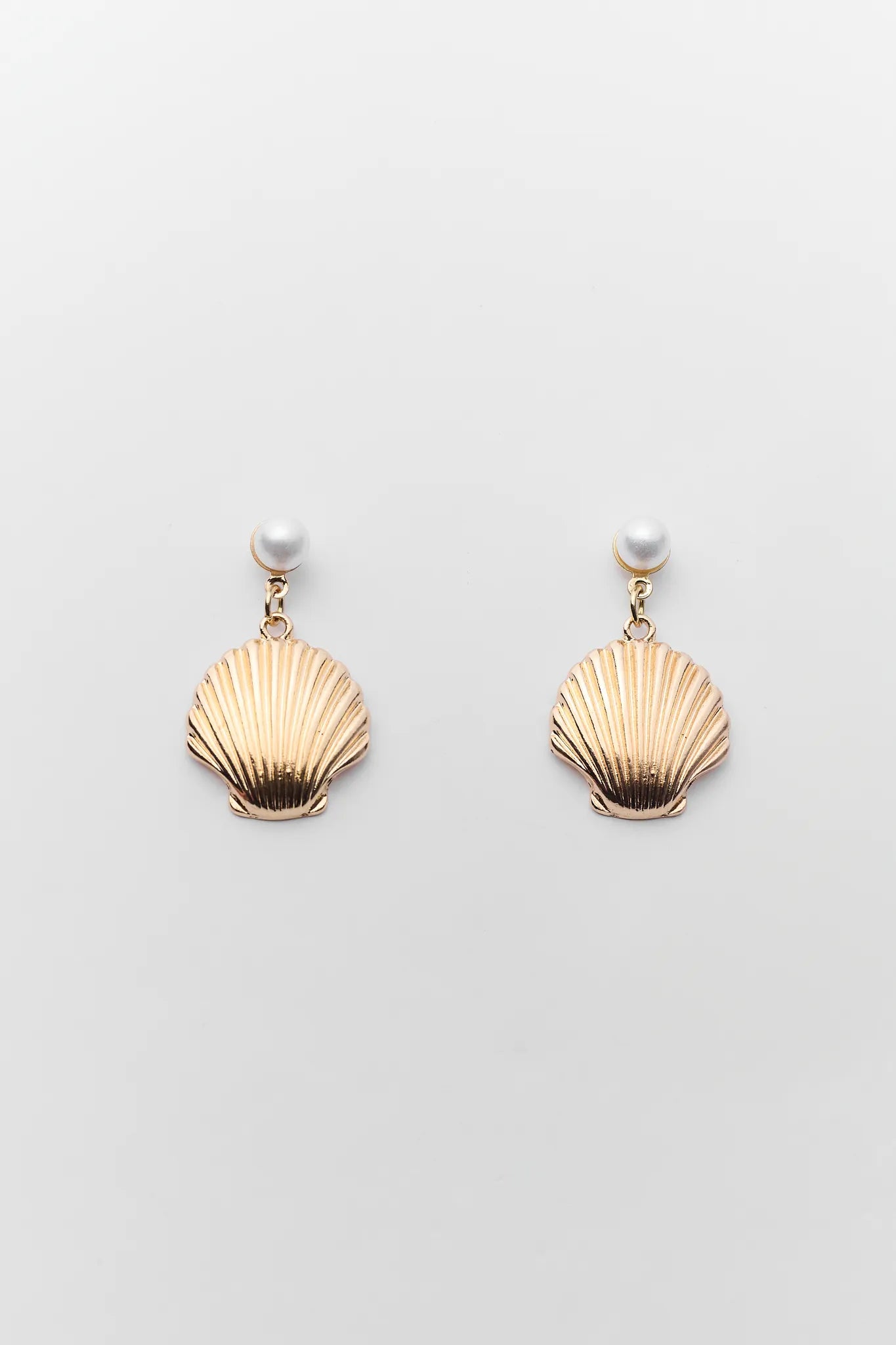 Gold shell-shaped earrings with pearl centers on a light gray background