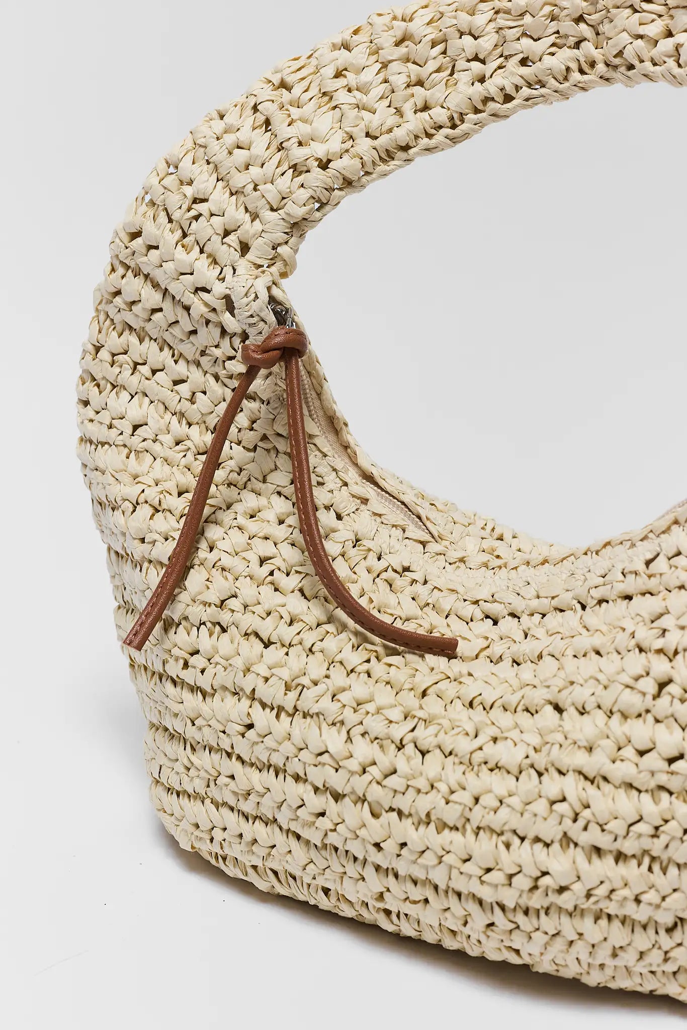 Beige woven bag with a brown strap on a light gray background