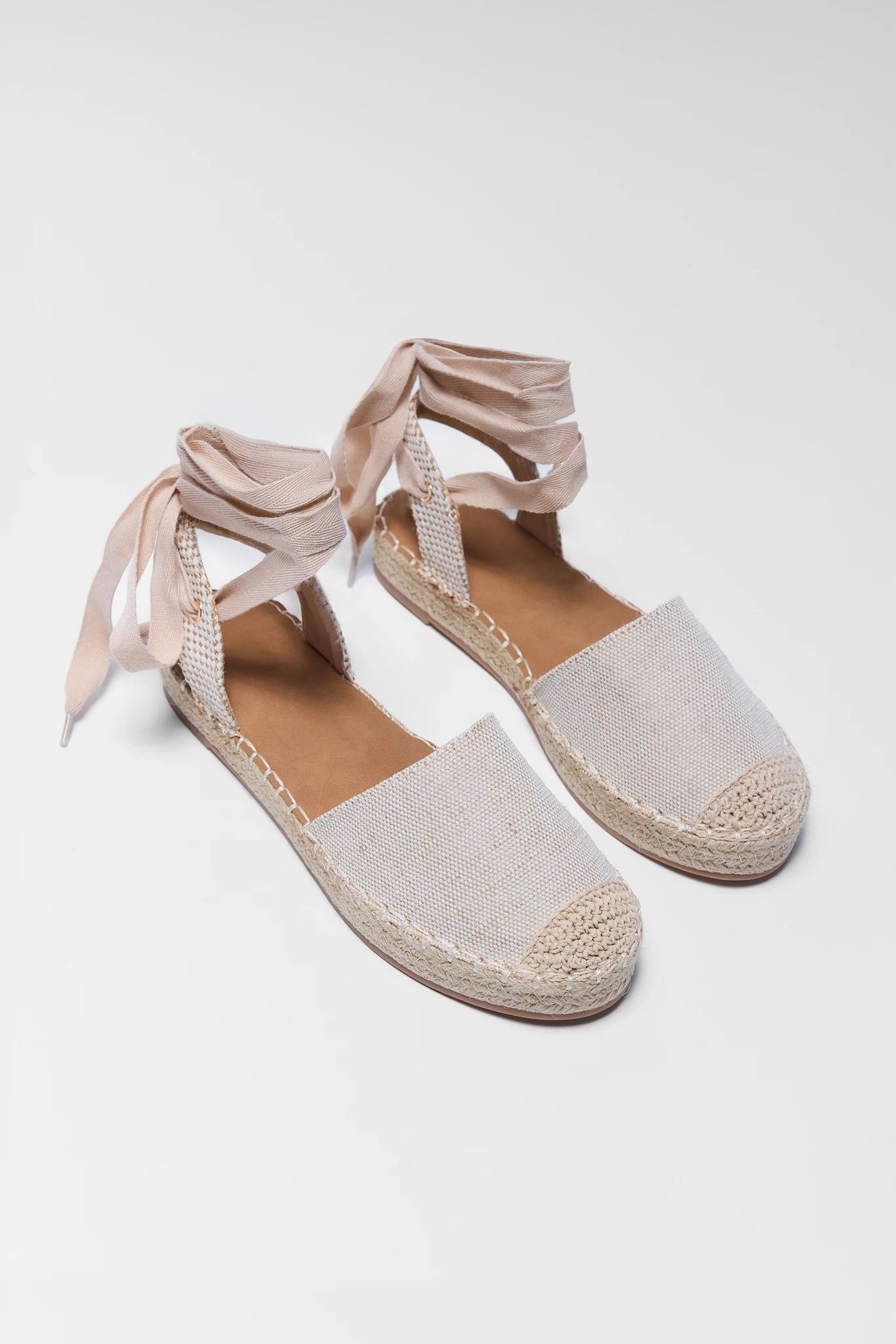 Pair of beige espadrilles with ribbon straps on a white background two